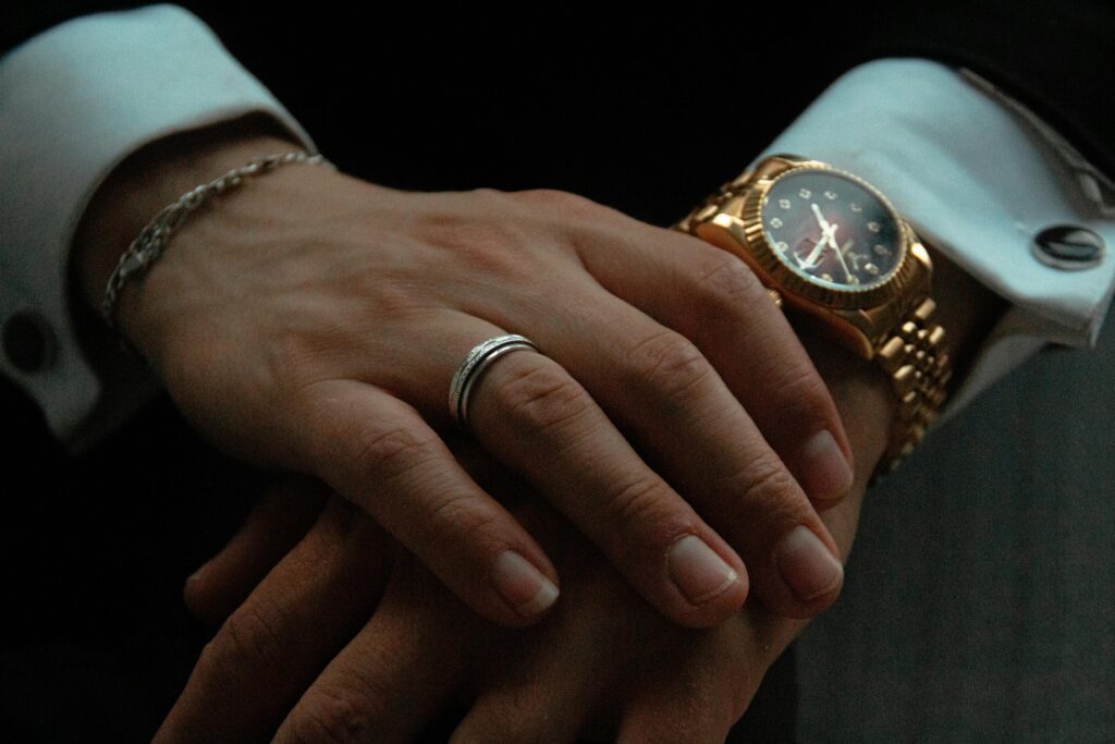 Close-up of a person's hands adorned with a stylish gold wristwatch and silver jewelry, showcasing elegance.